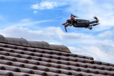 Side view of a black drone flying over roof