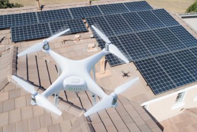 View of a white drone flying over roof with solar panels