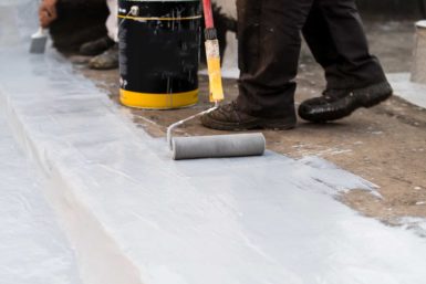 Close up view of a roofing worker applying a coating to a roof