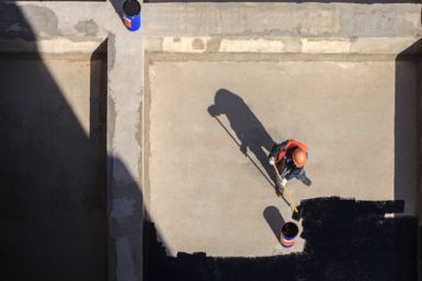 Roofer roller applying a blak roof coating